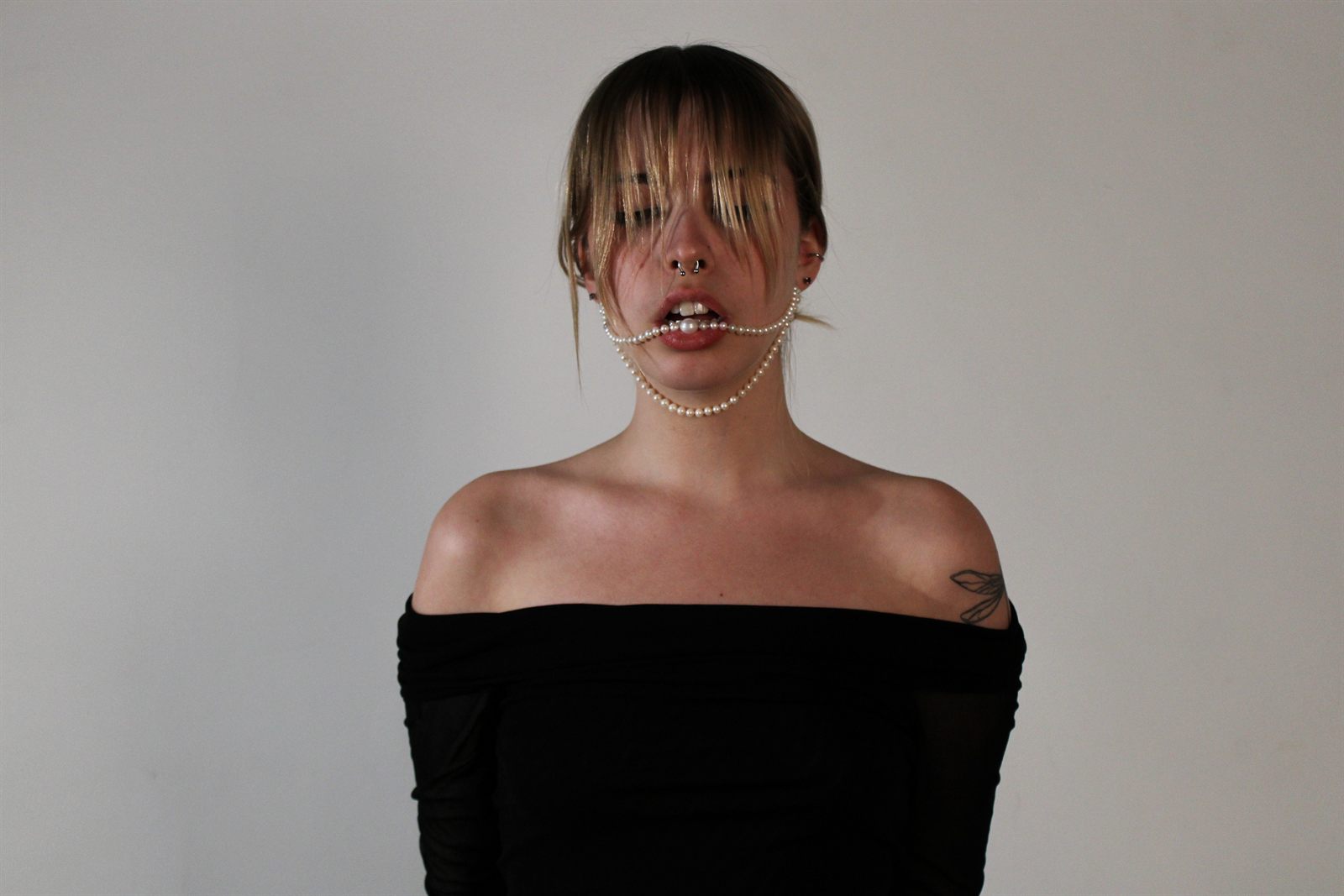 Directed portrait — a strand of pearls held in the mouth, on a grey backdrop