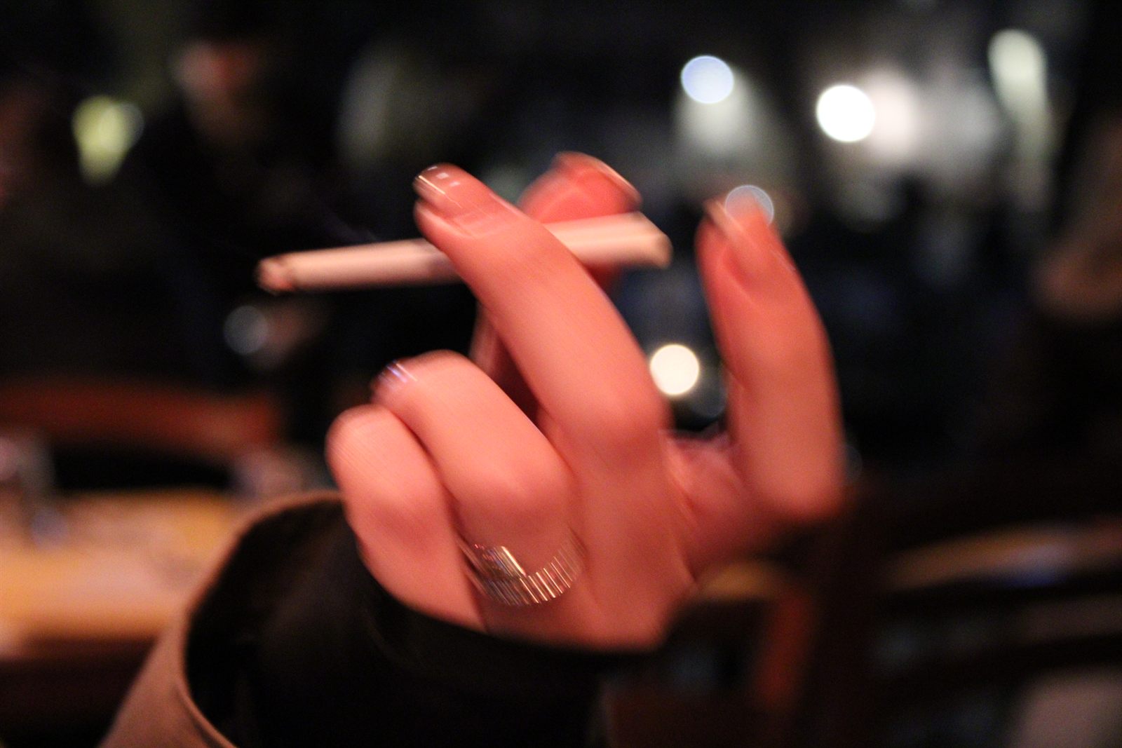 Street — a hand holding a cigarette, in a bar at night